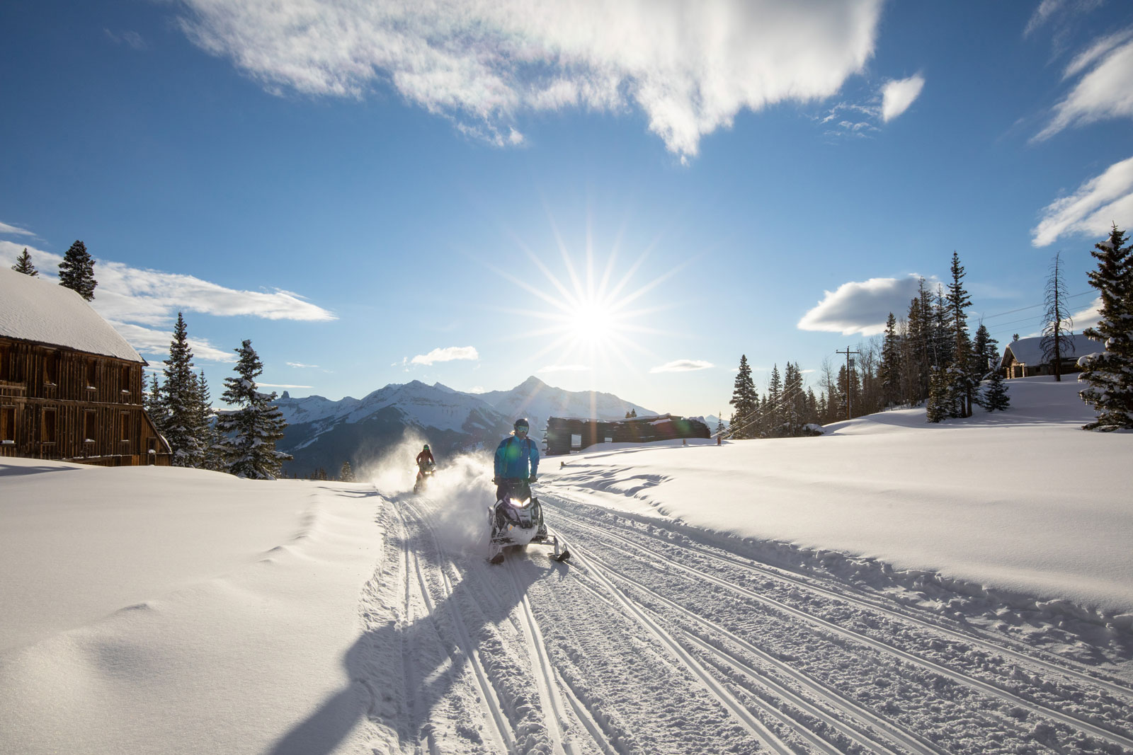 Snowmobilers make tracks underneath a sunny blue sky