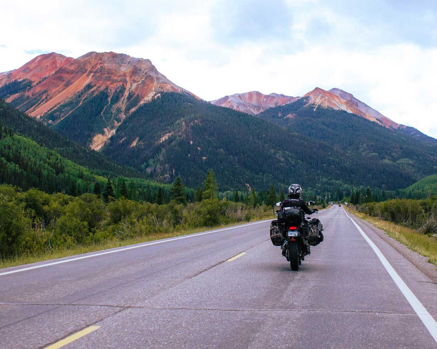 A motorcyclists rides on a paved road beneath a mountain range