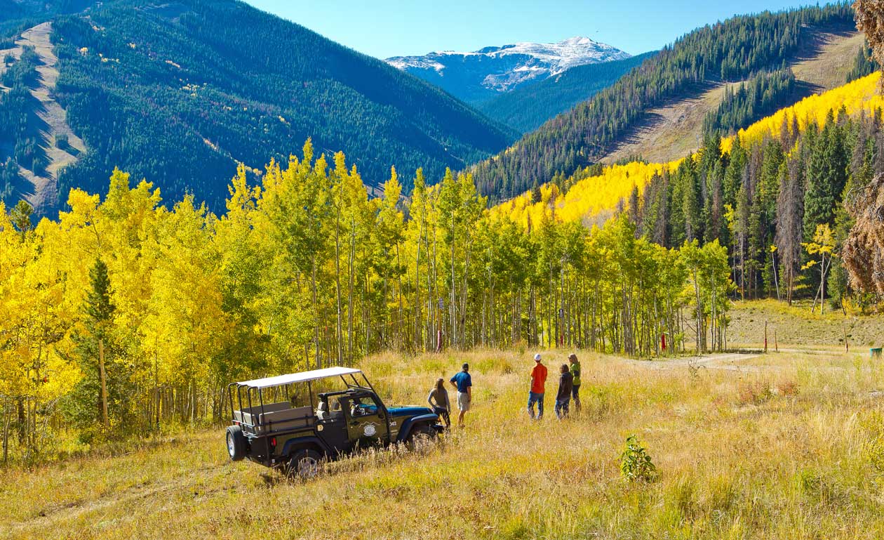 A Jeep is parked while it's passengers hike around a fall scene