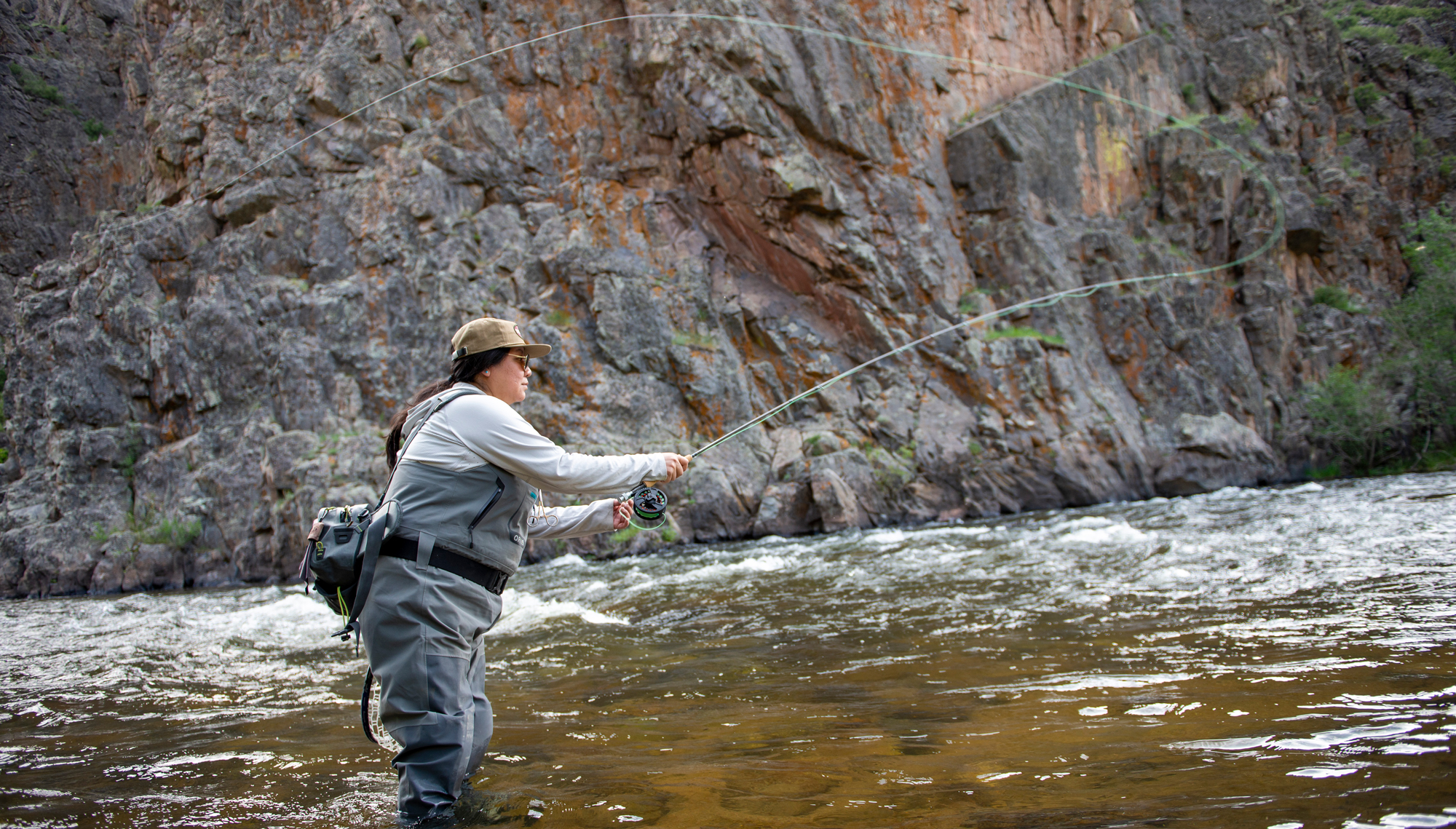 A person fly-fishes in the middle of a river flowing through a canyon in Almont, Colorado