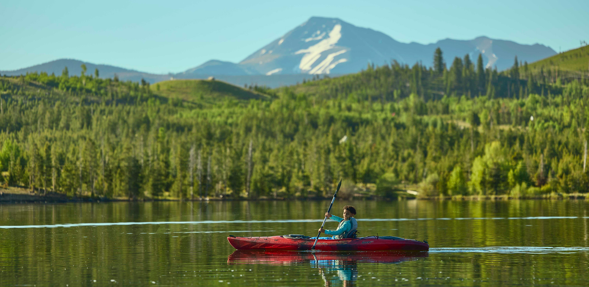 A person kayaks across a calm lake with mountains in the background in Frisco, Colorado