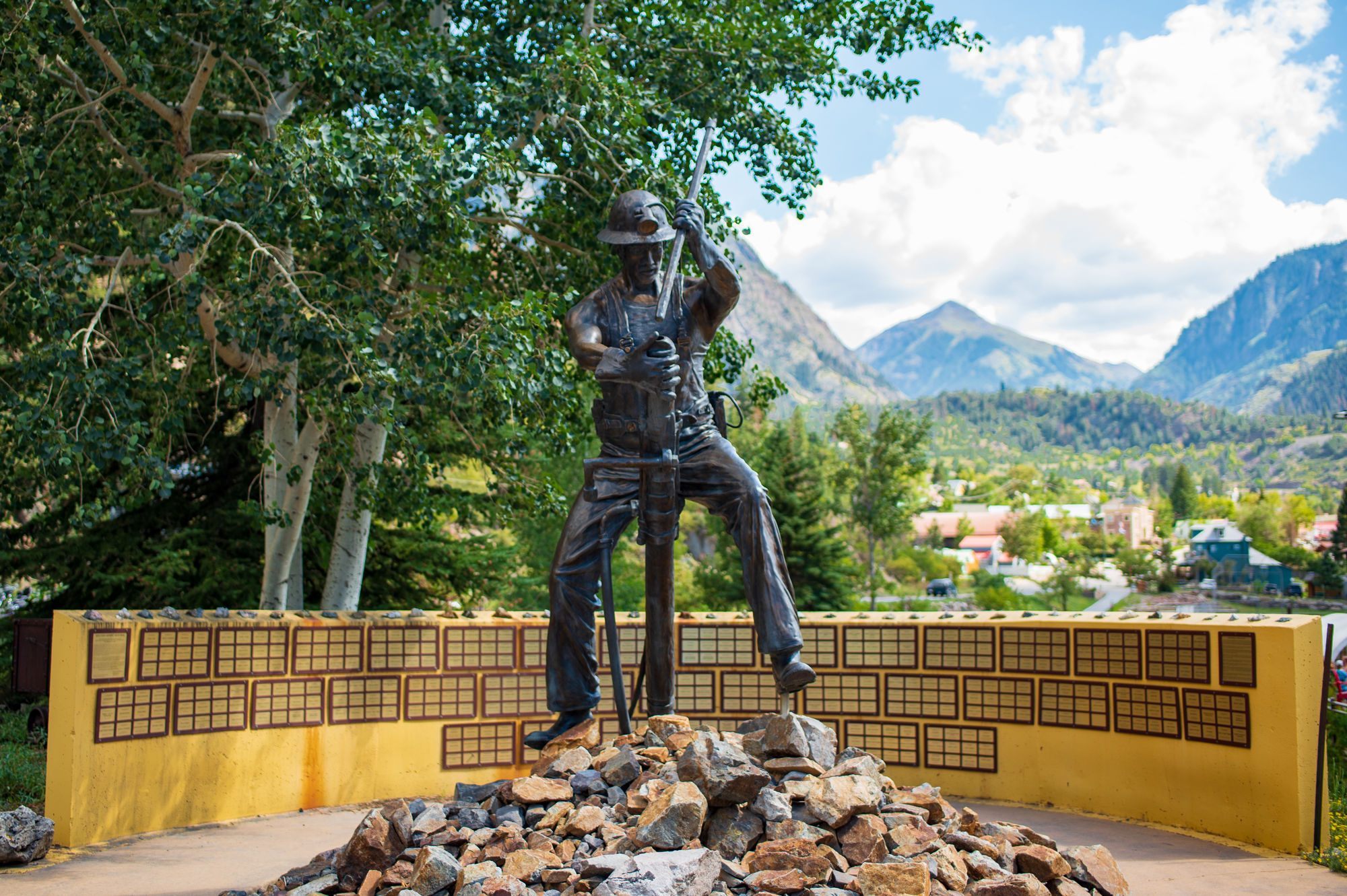 A statue of a miner surrounded by rocks with mountains in the background in Ouray, Colorado.