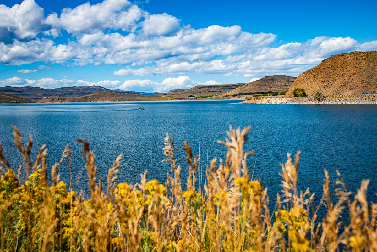 Boating on Blue Mesa Reservoir in Gunnison, Colorado on a sunny day with fluffy clouds filling the sky and rolling buttes in the background
