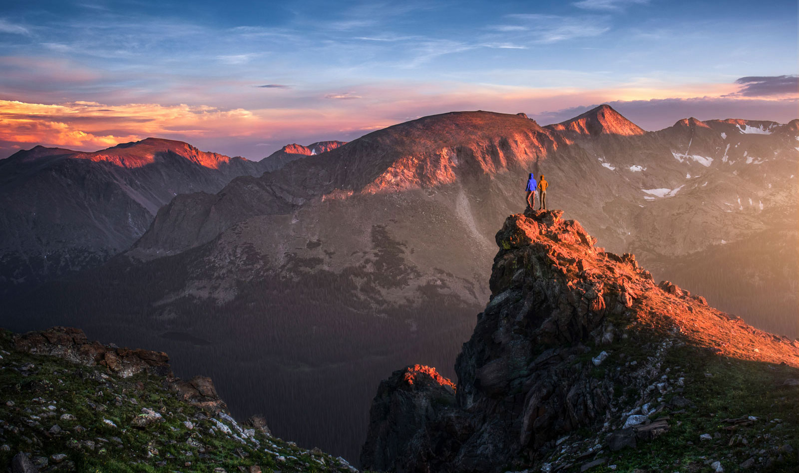 Two people stand on a ridge high above a mountain valley in Colorado