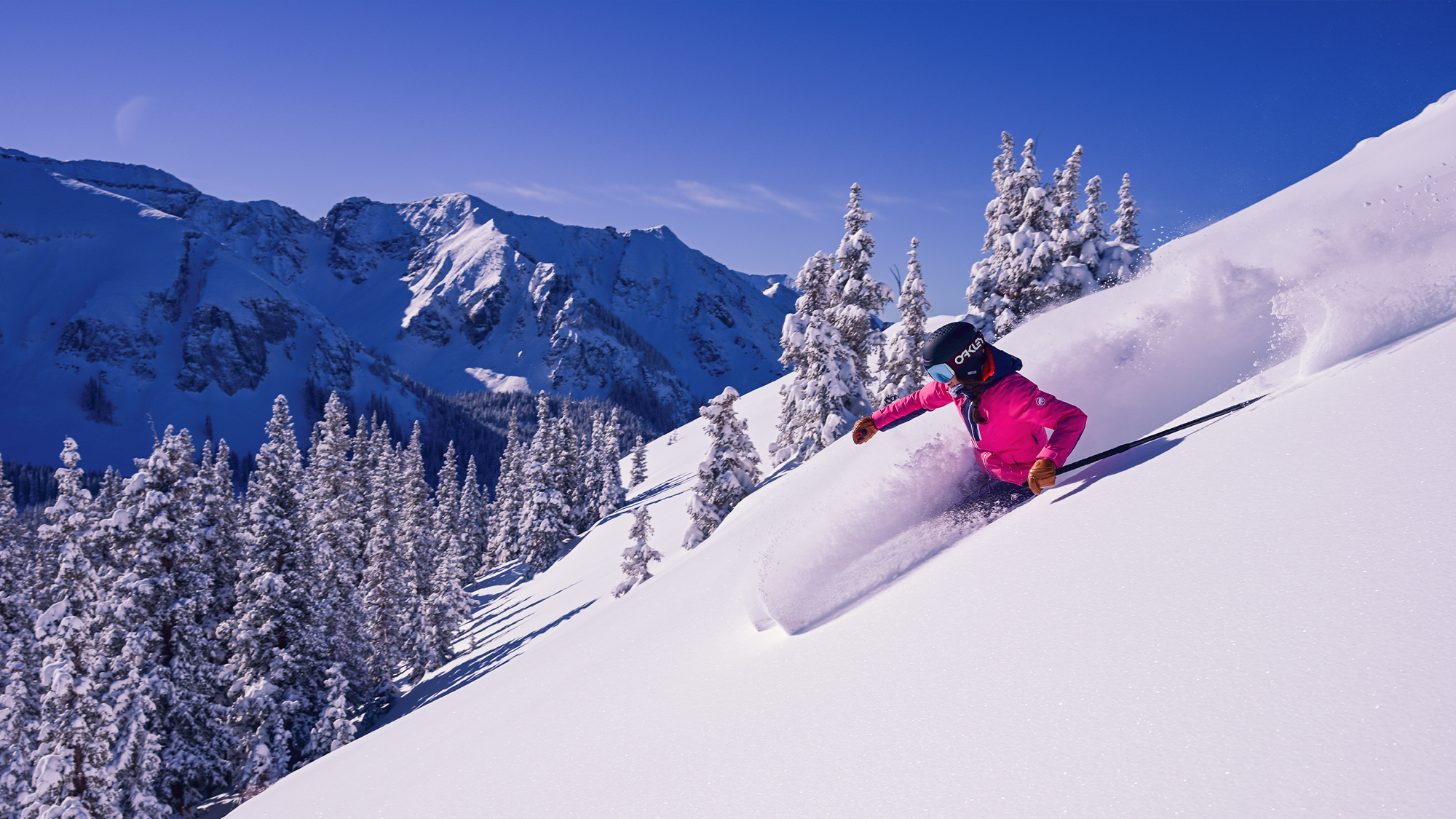 Skier wearing a helmet and pink coat on a downhill run through powdery mountain snow in Telluride, Colorado.